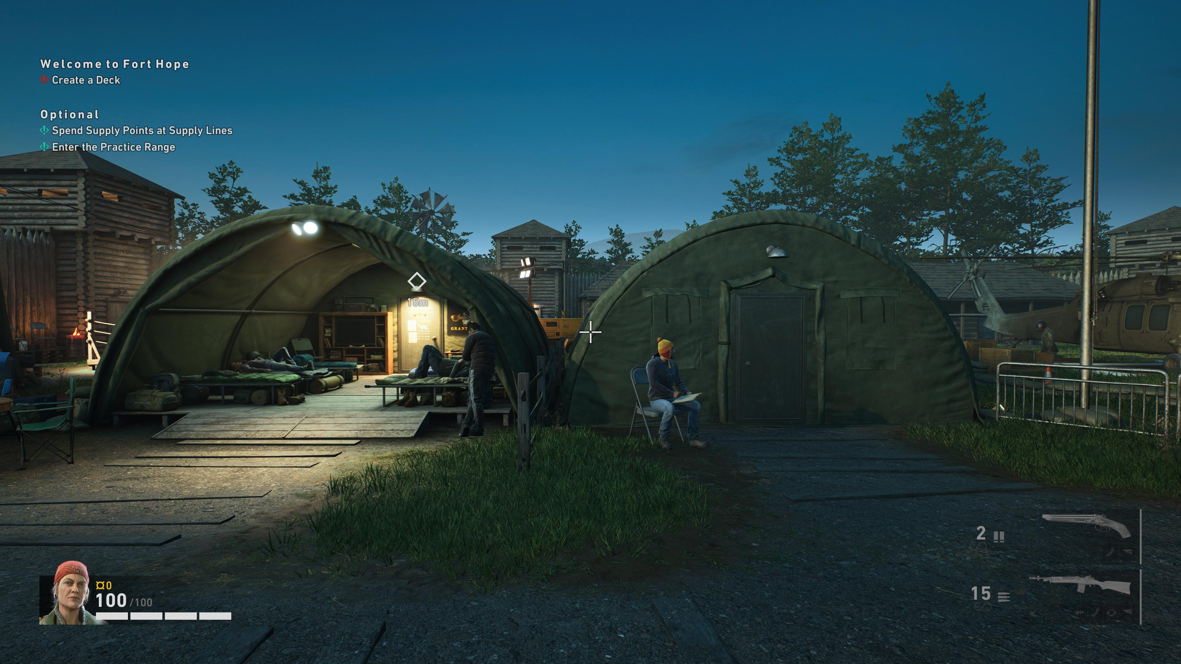 A screenshot from the game, showing Fort Hope, the place where the players start the game. The screenshot shows an area that looks like a military camp, with some barracks. The image has a firt person view. You can see a blue sky on the top. Almost nighttime. Some lights are on in one of the barracks and someone is seating next to the entrance of another barrack. There are game HUD elements on screen, like character health and current weapons. Two different shotguns, in this case.
